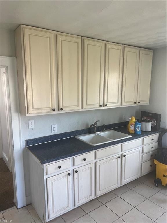 kitchen featuring light tile patterned floors, cream cabinets, dark countertops, and a sink