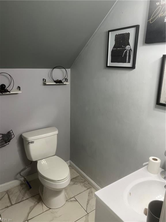 bathroom featuring lofted ceiling, toilet, vanity, baseboards, and marble finish floor