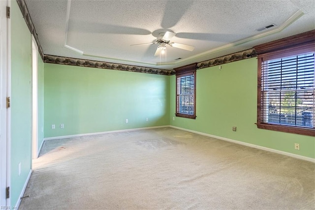 carpeted empty room with ceiling fan, a wealth of natural light, and a raised ceiling