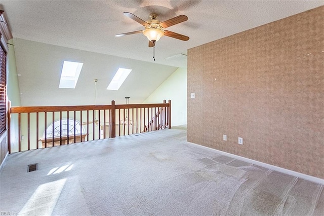 spare room featuring ceiling fan, carpet, lofted ceiling with skylight, and a textured ceiling