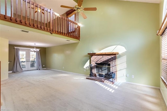 unfurnished living room featuring light carpet, french doors, a brick fireplace, and ceiling fan with notable chandelier