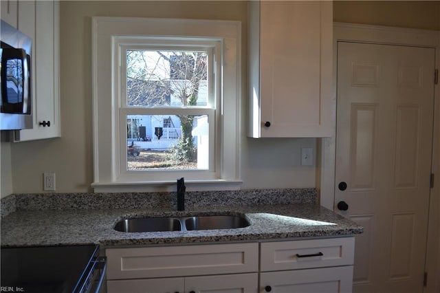 kitchen with light stone countertops, sink, white cabinets, and electric range oven