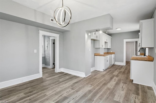 kitchen with hanging light fixtures, white cabinetry, butcher block countertops, and sink