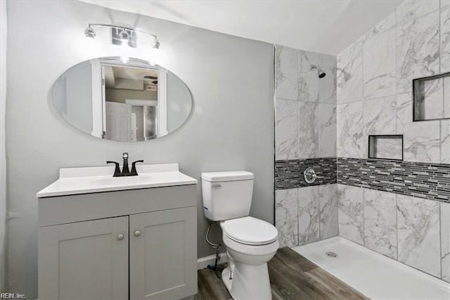 bathroom with hardwood / wood-style floors, toilet, vanity, and a tile shower