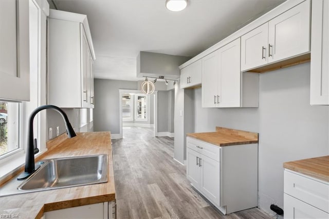 kitchen featuring wood counters, decorative light fixtures, white cabinetry, sink, and light wood-type flooring