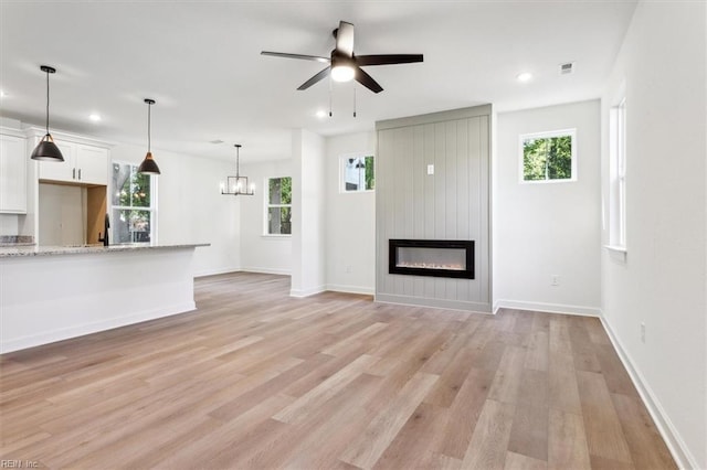 unfurnished living room featuring a fireplace, ceiling fan with notable chandelier, and light hardwood / wood-style flooring