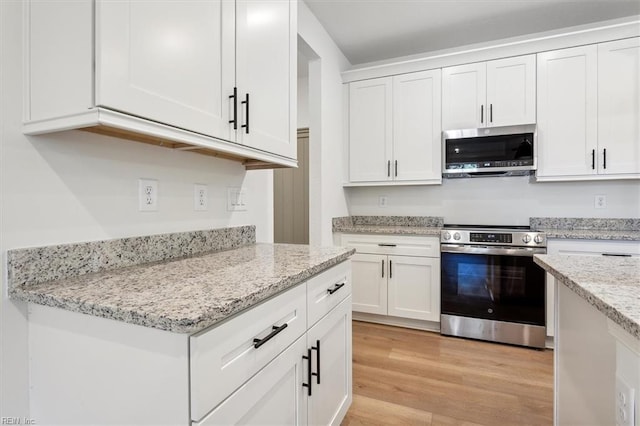 kitchen with light wood-type flooring, appliances with stainless steel finishes, white cabinetry, and light stone counters