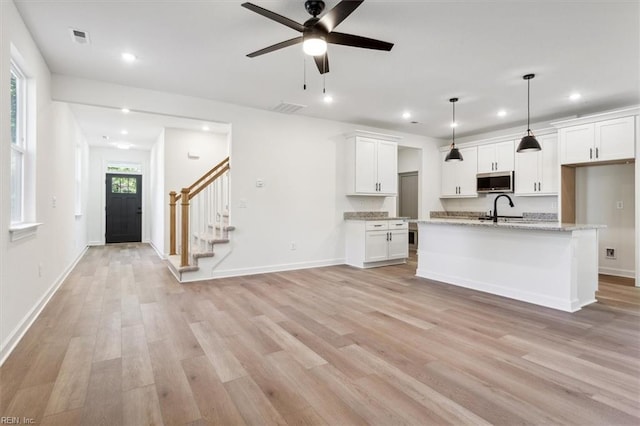 kitchen with pendant lighting, sink, a kitchen island with sink, light stone countertops, and white cabinets