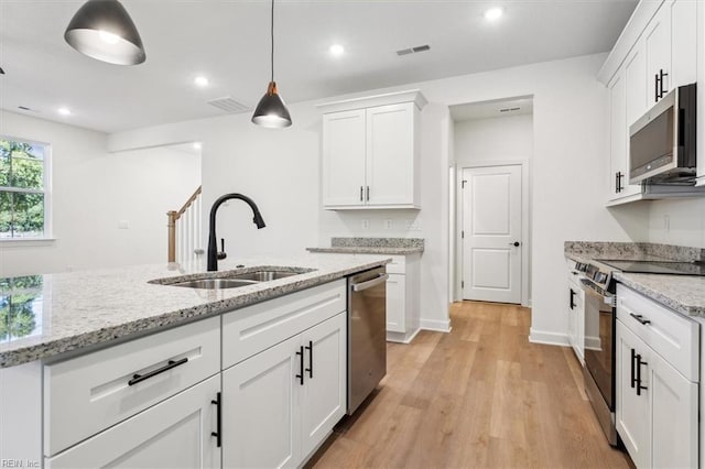 kitchen with white cabinets, appliances with stainless steel finishes, sink, and light stone counters