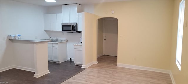 kitchen with baseboards, arched walkways, stainless steel microwave, wood finished floors, and light countertops