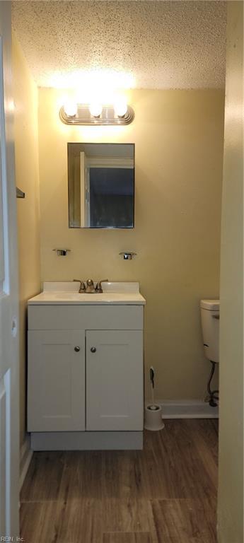 half bathroom featuring toilet, a textured ceiling, wood finished floors, and vanity