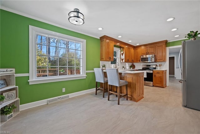 kitchen with a kitchen bar, kitchen peninsula, appliances with stainless steel finishes, ornamental molding, and sink