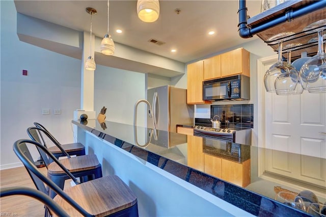 kitchen with light hardwood / wood-style flooring, hanging light fixtures, light brown cabinets, appliances with stainless steel finishes, and kitchen peninsula