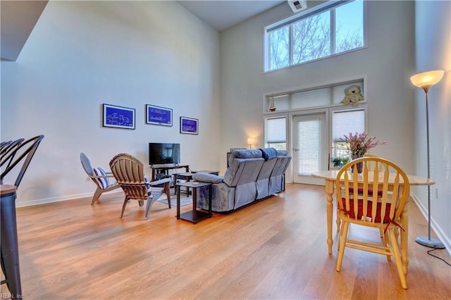 living room with a towering ceiling, plenty of natural light, and light wood-type flooring