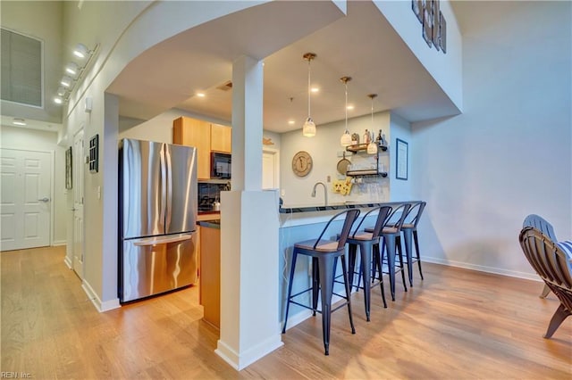 kitchen with stainless steel fridge, a kitchen breakfast bar, light hardwood / wood-style floors, kitchen peninsula, and light brown cabinets