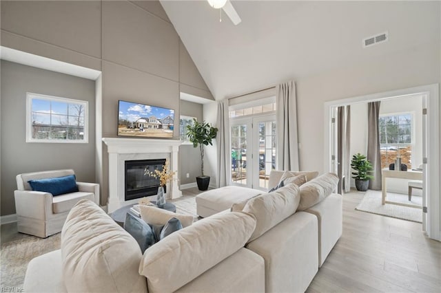 living room with a high end fireplace, light hardwood / wood-style flooring, and high vaulted ceiling