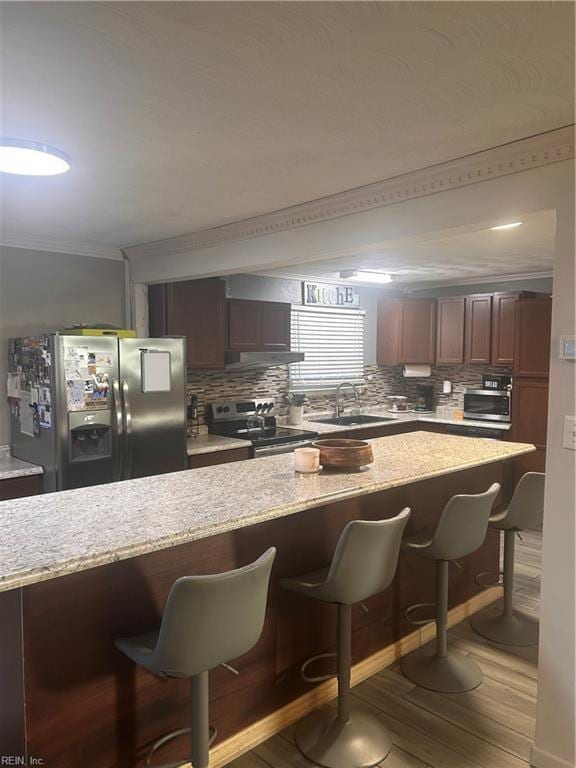 kitchen featuring stainless steel appliances, sink, ornamental molding, hardwood / wood-style flooring, and a breakfast bar