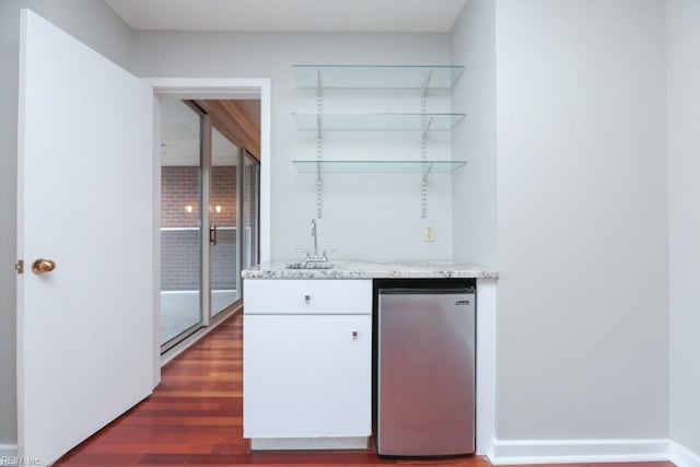 bar featuring sink, stainless steel refrigerator, light stone counters, white cabinets, and dark hardwood / wood-style flooring