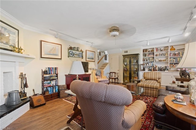 living area featuring rail lighting, built in features, ornamental molding, and light wood-type flooring