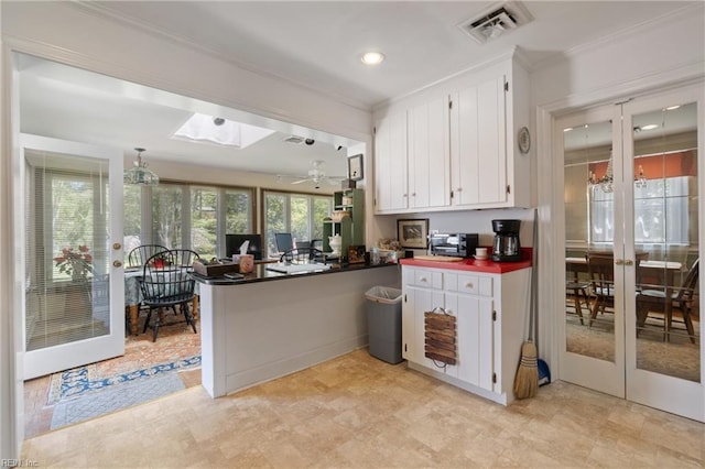 kitchen featuring kitchen peninsula, crown molding, a skylight, white cabinets, and french doors