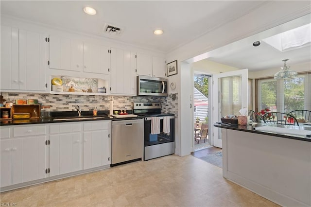 kitchen with a skylight, white cabinetry, stainless steel appliances, decorative backsplash, and sink