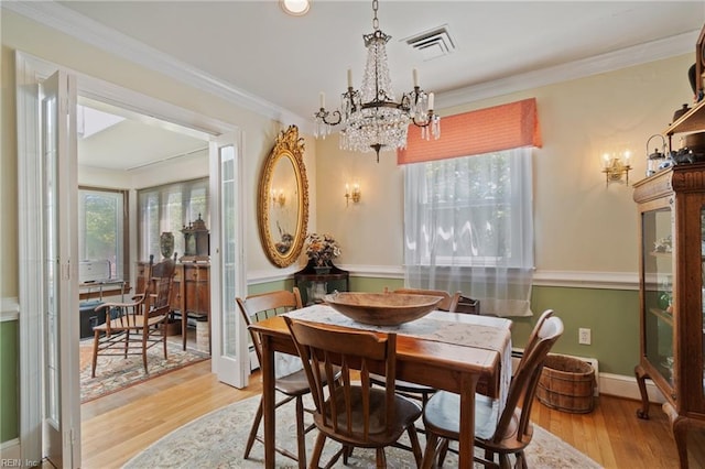 dining space with light hardwood / wood-style flooring, ornamental molding, and a notable chandelier