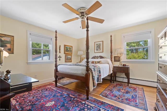 bedroom featuring ceiling fan, multiple windows, a baseboard heating unit, and light wood-type flooring