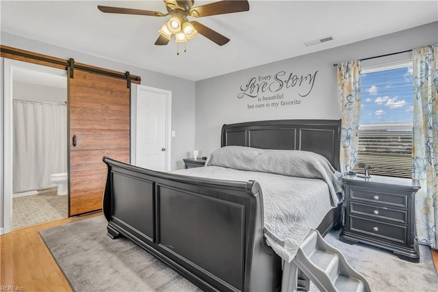 bedroom featuring ceiling fan, wood-type flooring, ensuite bath, and a barn door