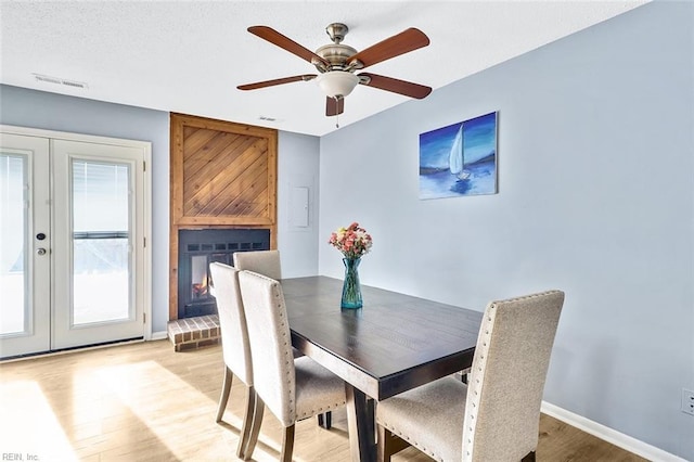 dining room featuring a brick fireplace, french doors, ceiling fan, and light wood-type flooring