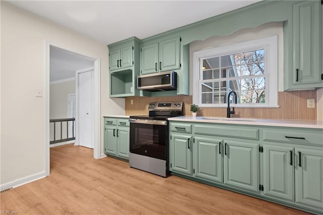 kitchen with sink, light wood-type flooring, green cabinets, and appliances with stainless steel finishes