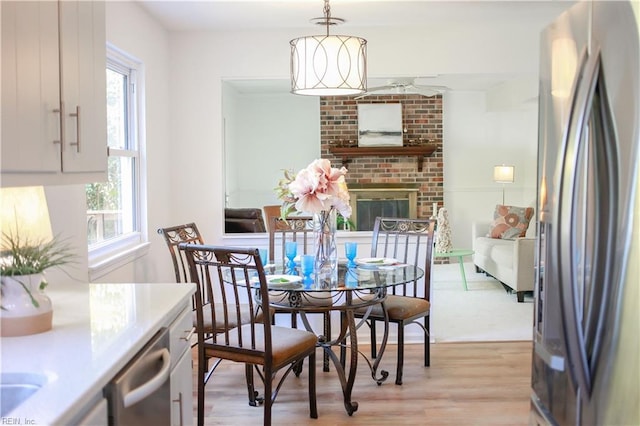 dining room featuring light wood-type flooring, a brick fireplace, and a wealth of natural light