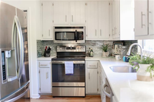 kitchen with sink, backsplash, white cabinets, and stainless steel appliances