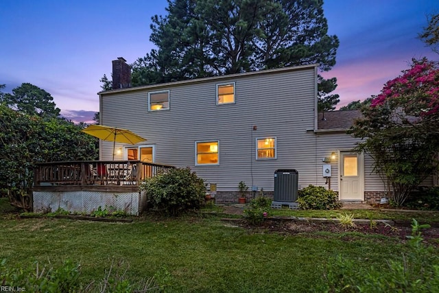 back house at dusk featuring a wooden deck, a yard, and central AC unit