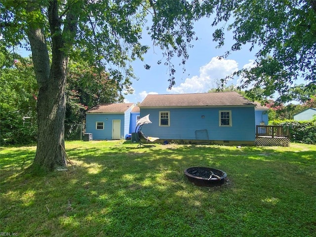 rear view of property with a lawn, an outdoor fire pit, a deck, and an outdoor structure