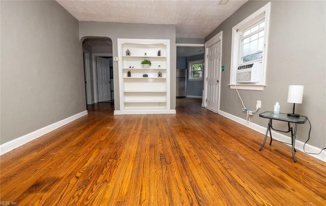 unfurnished living room with a textured ceiling, cooling unit, hardwood / wood-style floors, and built in shelves