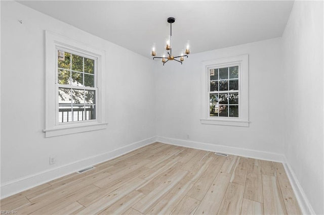 spare room featuring a chandelier and light wood-type flooring