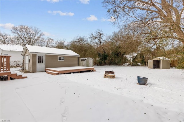 snow covered house featuring a fire pit, a deck, and a storage unit