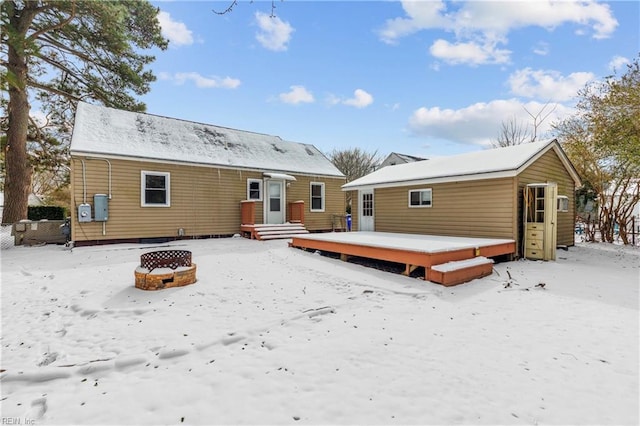 snow covered house with a wooden deck and an outdoor fire pit