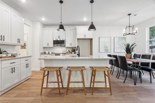 kitchen with an island with sink, white cabinets, sink, and light stone counters