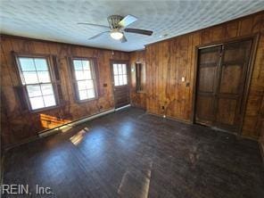 unfurnished room with dark wood-type flooring, ceiling fan, and wooden walls