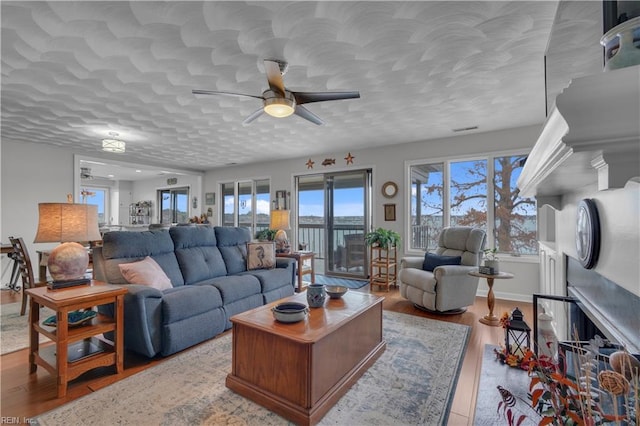 living room featuring a textured ceiling, ceiling fan, a fireplace, and light hardwood / wood-style flooring