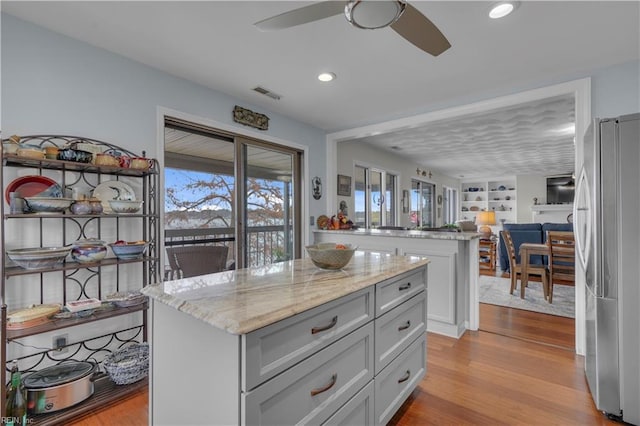 kitchen with a kitchen island, stainless steel fridge, built in features, light wood-type flooring, and light stone counters