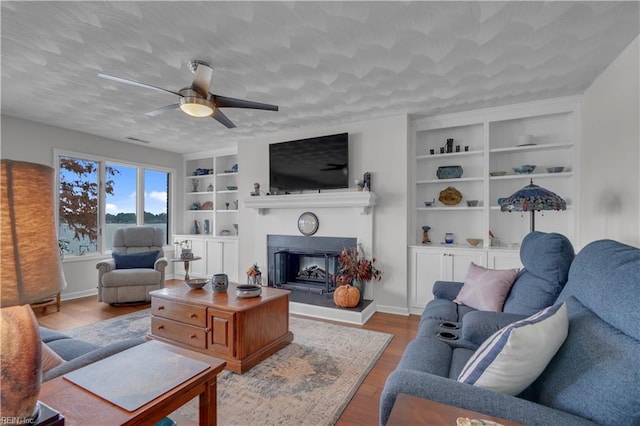 living room featuring a textured ceiling, ceiling fan, light hardwood / wood-style floors, and built in features