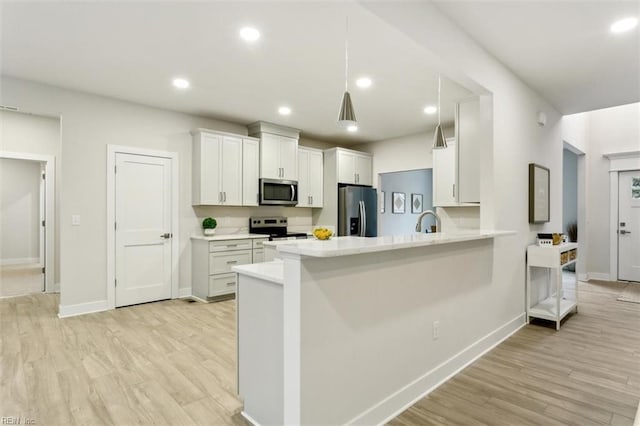 kitchen with appliances with stainless steel finishes, white cabinets, light hardwood / wood-style floors, and kitchen peninsula