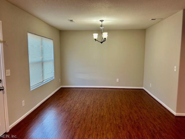 spare room with a textured ceiling, dark hardwood / wood-style floors, a chandelier, and a healthy amount of sunlight