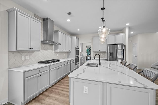 kitchen featuring pendant lighting, sink, wall chimney exhaust hood, stainless steel appliances, and a spacious island