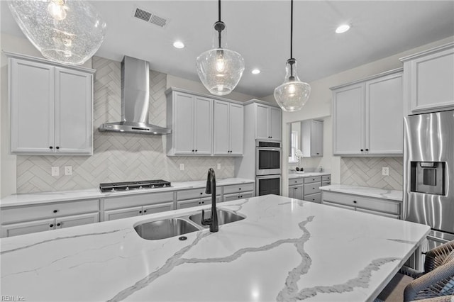 kitchen with wall chimney range hood, light stone countertops, hanging light fixtures, and appliances with stainless steel finishes