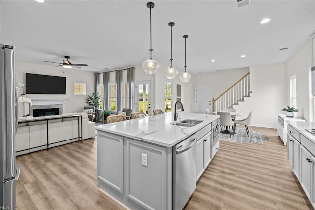 kitchen with sink, stainless steel appliances, light stone countertops, an island with sink, and decorative light fixtures