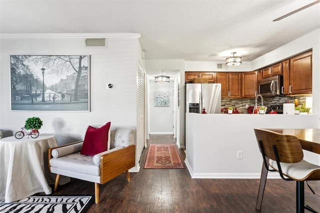 kitchen featuring dark wood-type flooring, appliances with stainless steel finishes, ornamental molding, and tasteful backsplash