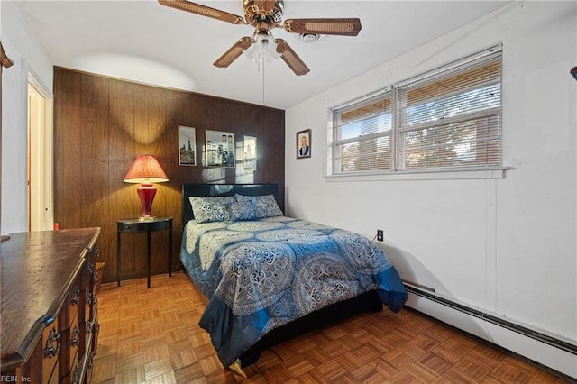 bedroom with wooden walls, a baseboard heating unit, dark parquet floors, and ceiling fan